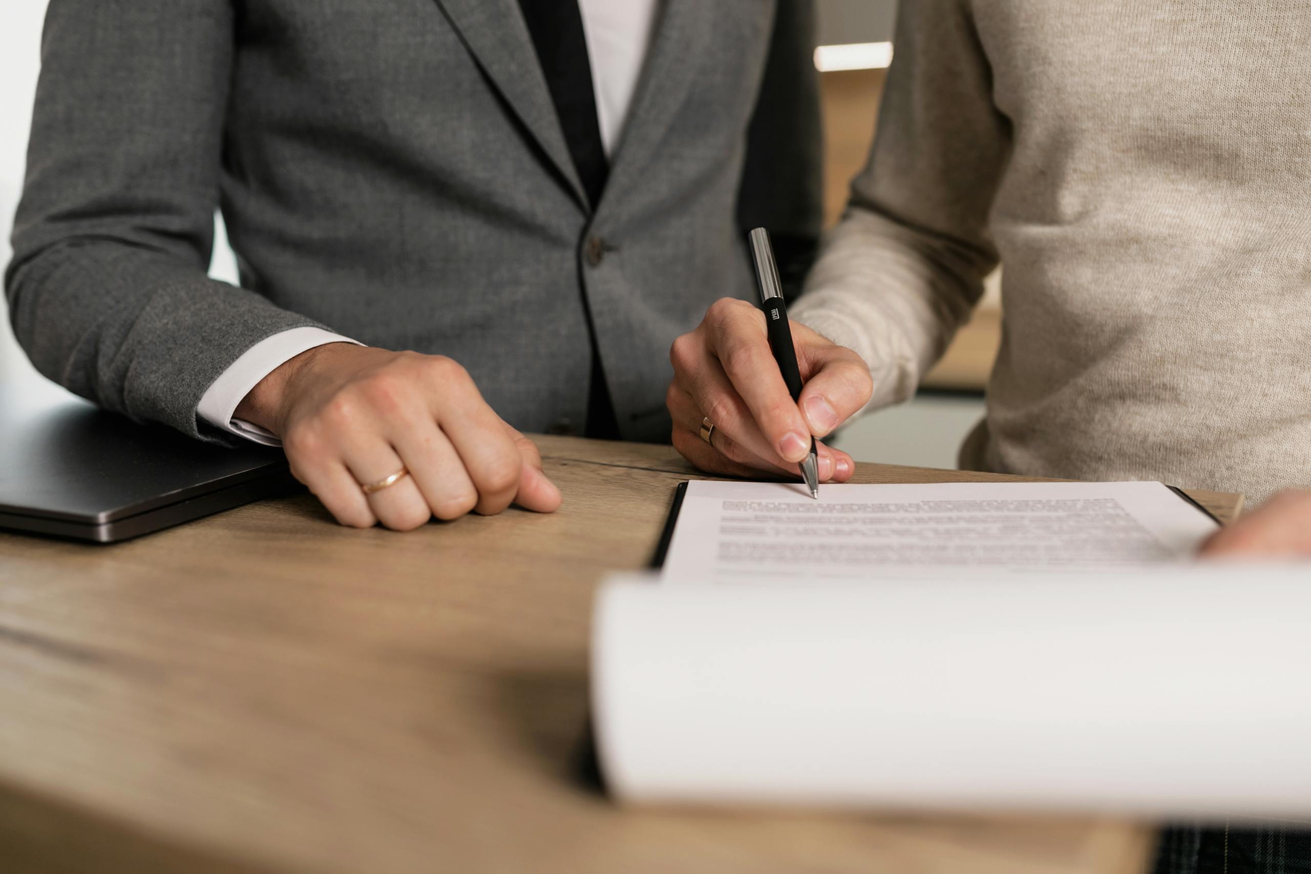 Close-up of businessmen signing documents at a wooden table in an office.