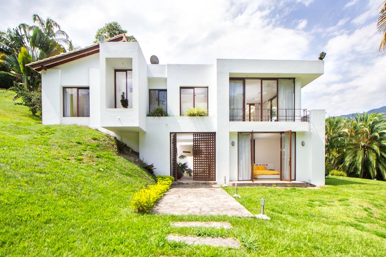 A contemporary white house surrounded by lush greenery on a hillside, showcasing modern architecture.